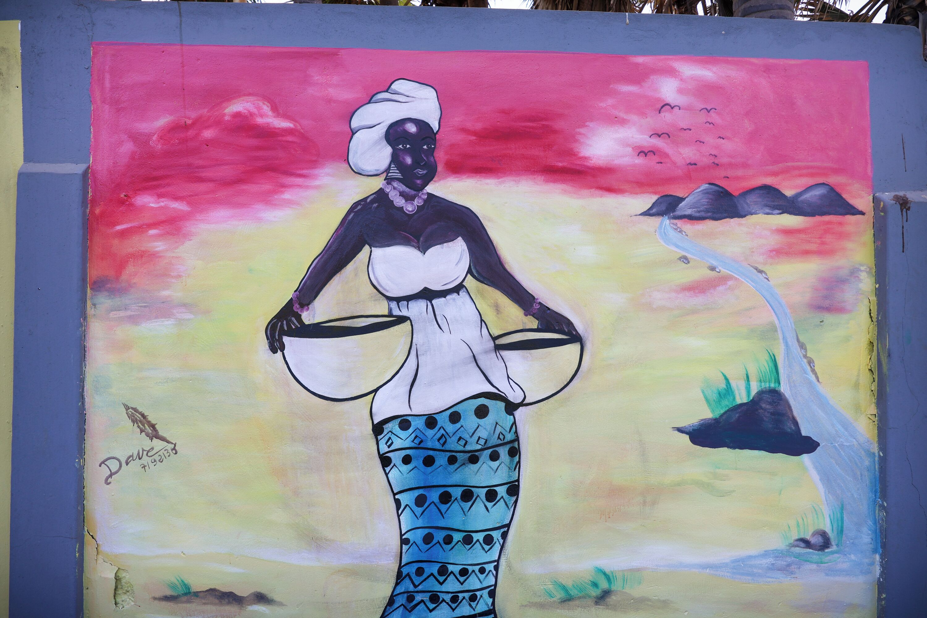 A mural of a woman holding two bowls, painted on a wall with a sunset background.