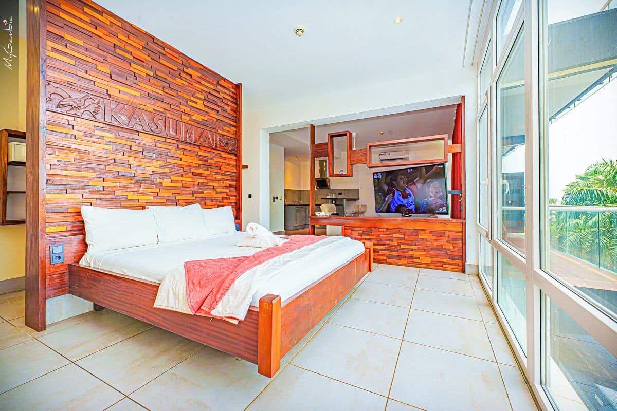 A modern bedroom with a wooden headboard, a large bed, a TV, and a balcony with a view.