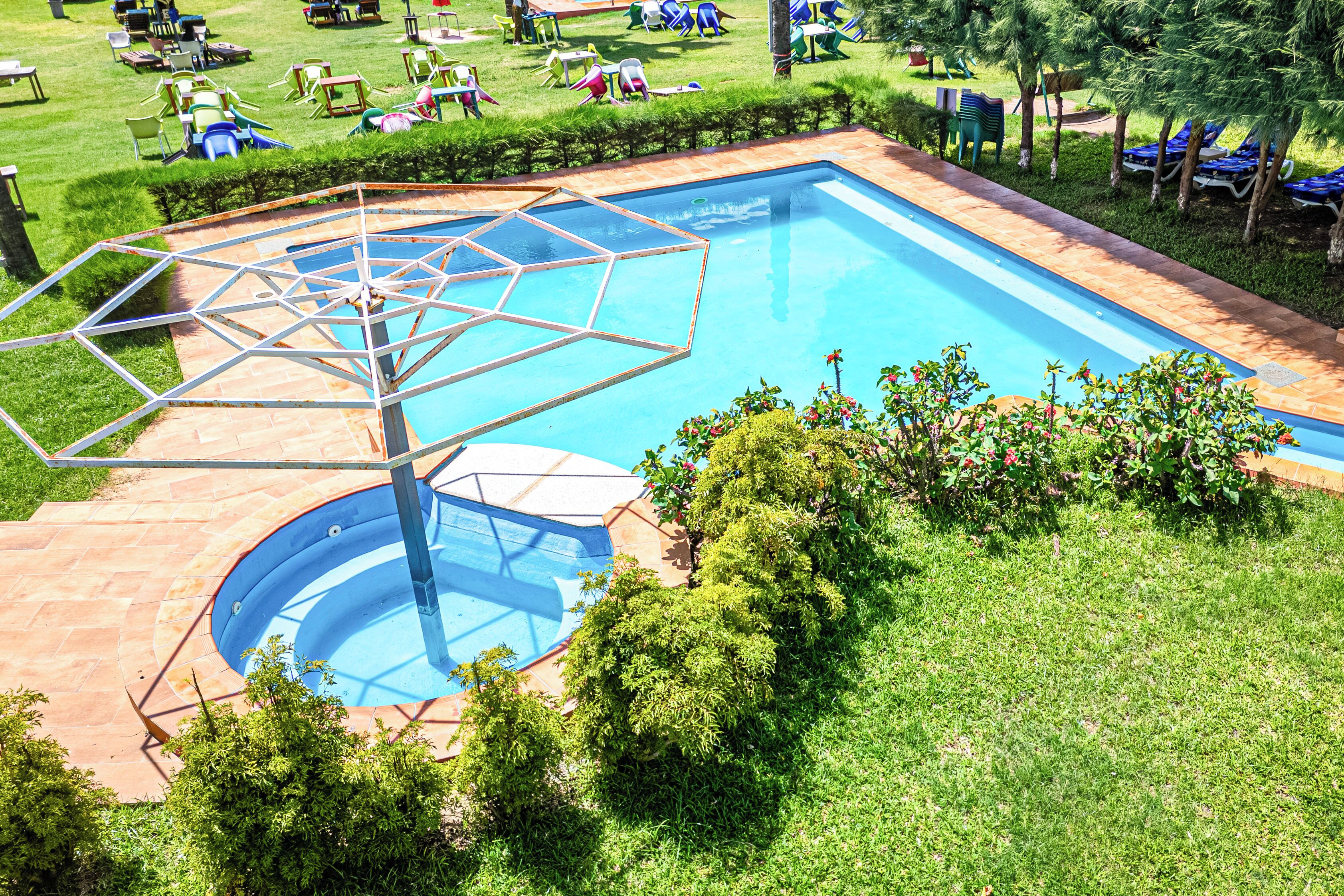 Una piscina con sombrilla, rodeada de sillas de jardín y sombrillas, y un césped bien cuidado.