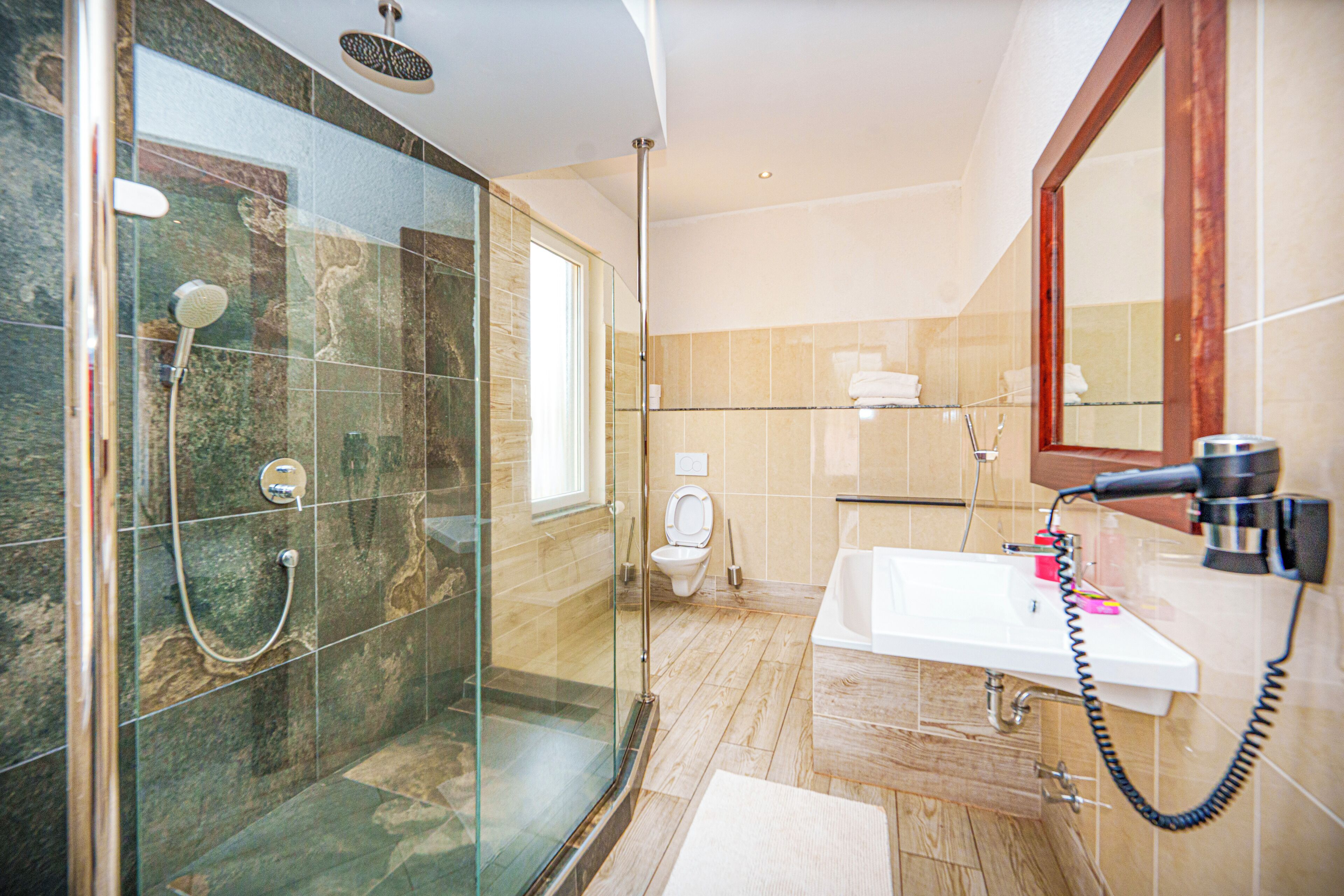 Un baño moderno con ducha envuelta en vidrio, un lavabo blanco y un espejo grande.