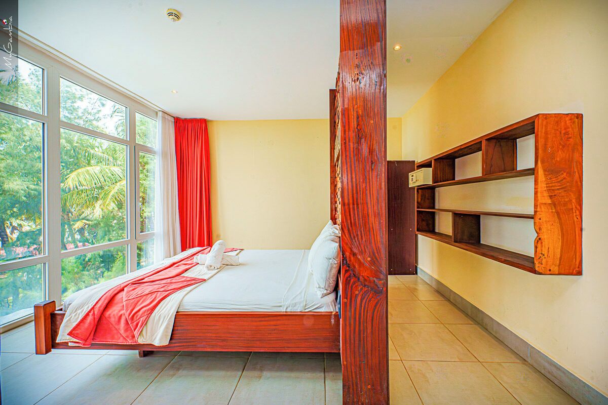 Un dormitorio con un ventanal amplio, una cama, una estantería de madera y una cortina roja.