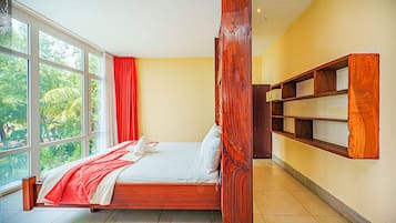 Un dormitorio con un ventanal amplio, una cama, una estantería de madera y una cortina roja.
