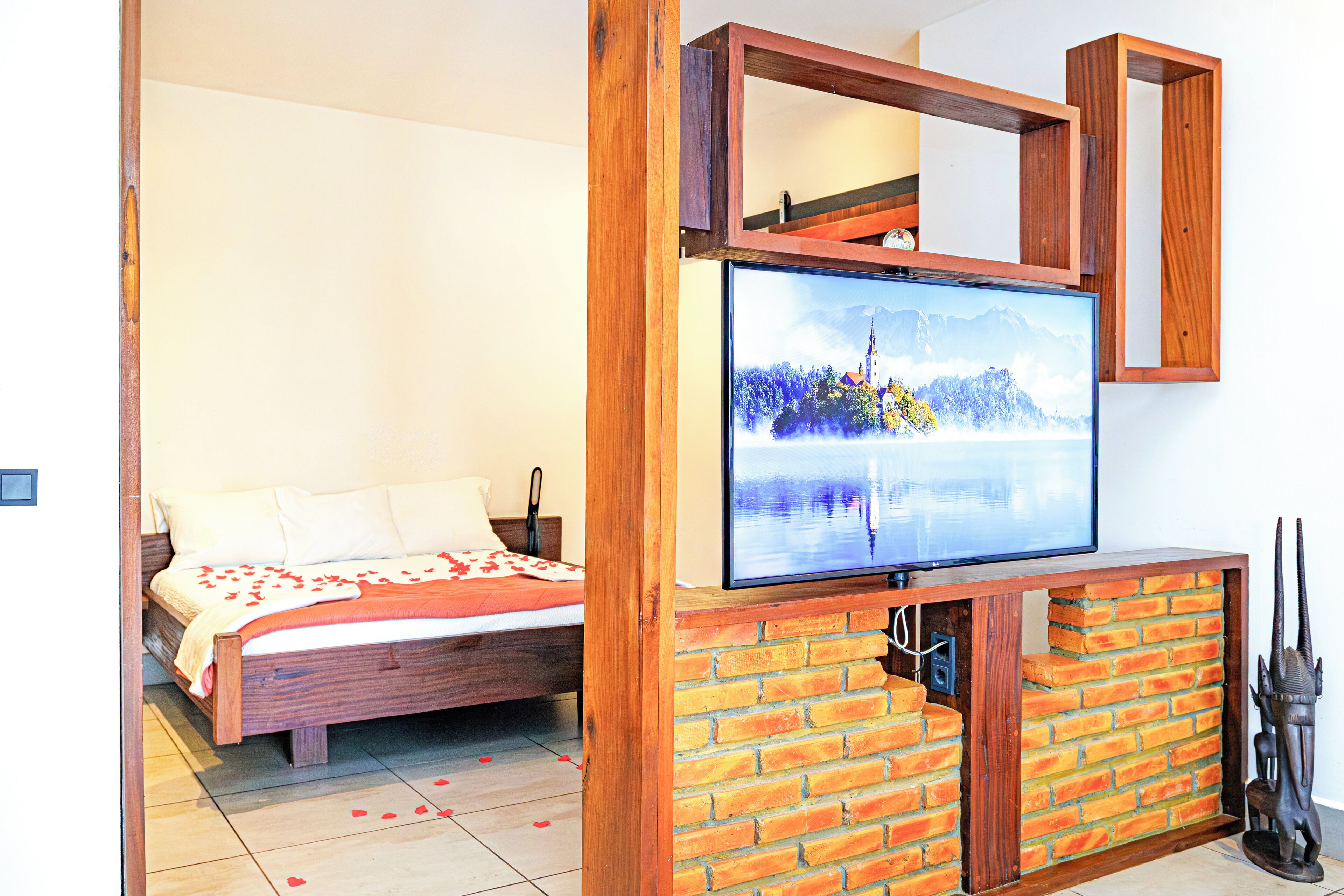 Un dormitorio con una cama, un televisor montado en una pared de ladrillo y un marco de madera encima del televisor.