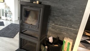 Un salon moderne avec un poêle à bois noir, un tapis gris et un mur en pierre.