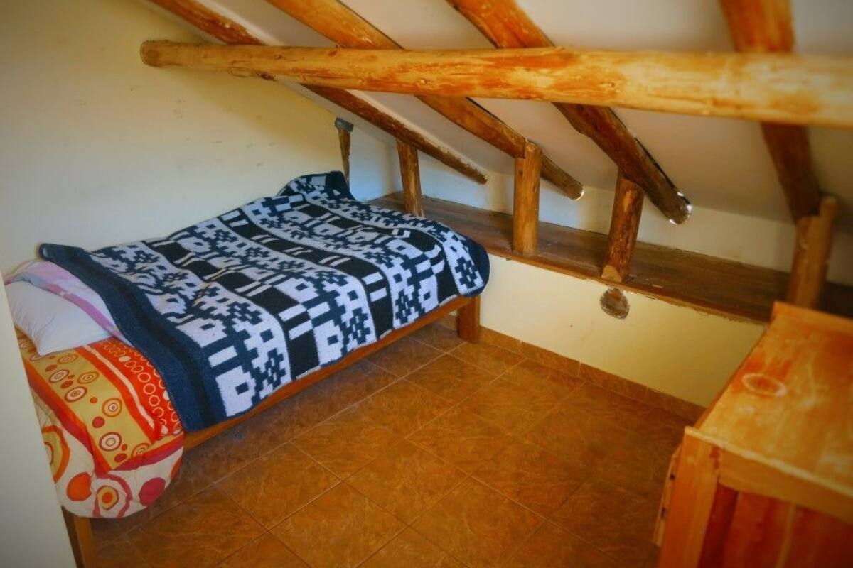 A small, cozy room with a wooden bed and a sloped ceiling.