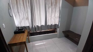 Een kleine kamer met een houten bureau, een raam met gordijnen en een betegelde vloer.