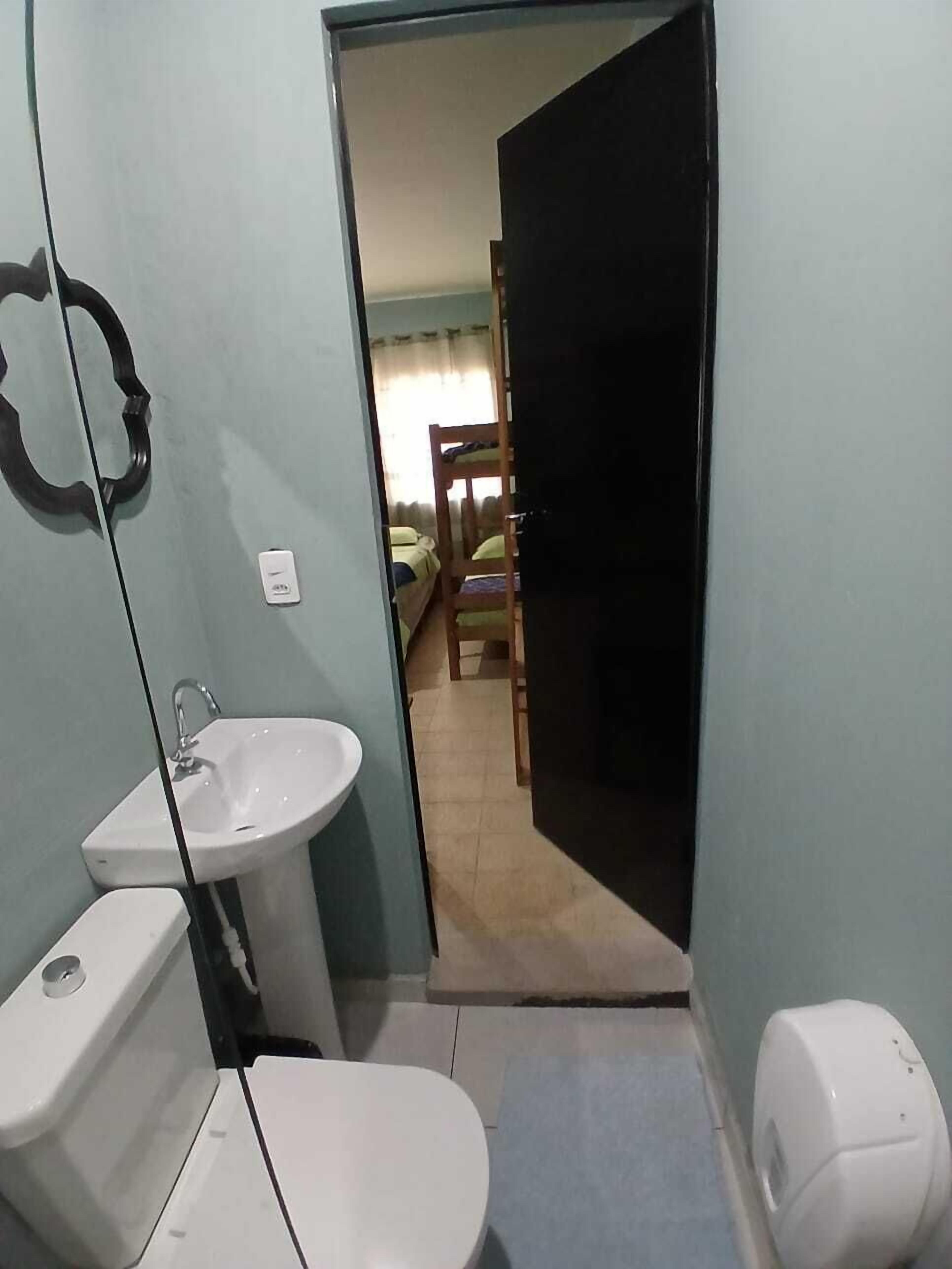 Un baño pequeño con lavamanos, inodoro y bidé. Un espejo cuelga de la pared, y una puerta da paso a un dormitorio con literas.