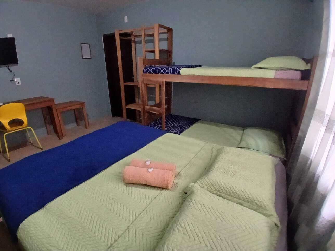A dormitory room with bunk beds, a desk, a chair, and a television.
