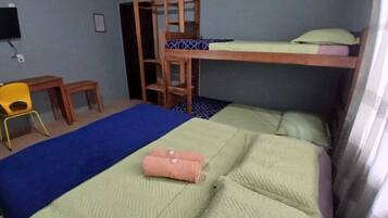 A dormitory room with bunk beds, a desk, a chair, and a television.