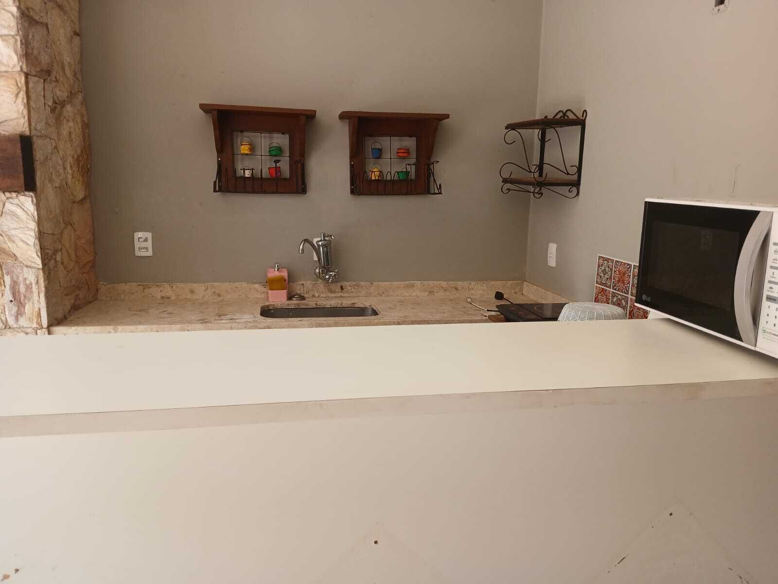 A kitchen with a stone accent wall, two wooden medicine cabinets, a sink with a soap dispenser, and a microwave.