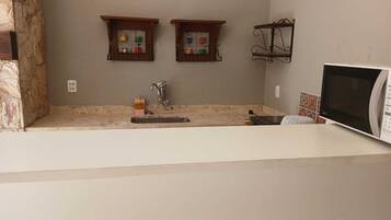 A kitchen with a stone accent wall, two wooden medicine cabinets, a sink with a soap dispenser, and a microwave.