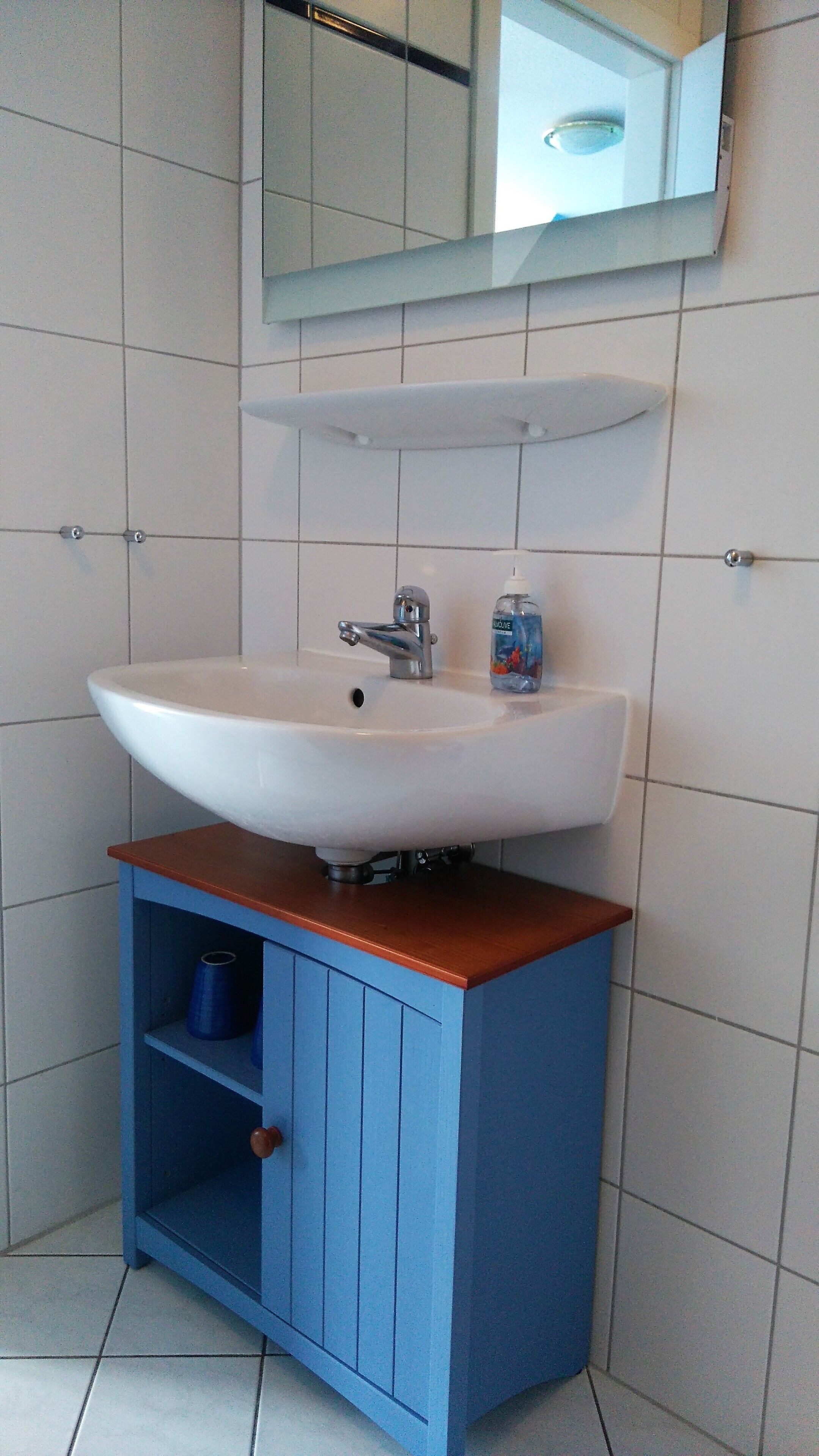 A bathroom with a white sink, blue cabinet, and a mirror above.