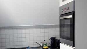 Una cocina moderna con armarios blancos, horno empotrado y cafetera en la encimera.