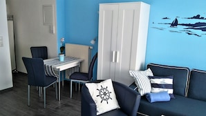 Una habitación con pared azul, un armario blanco, una mesa de comedor con sillas y un sofá con almohadones de temática náutica.