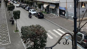 Un hotel de varios pisos con balcones, vista a la calle y una torre histórica al fondo.