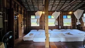 A room with wooden walls and a sloped ceiling, featuring three beds with white linens and mosquito nets.