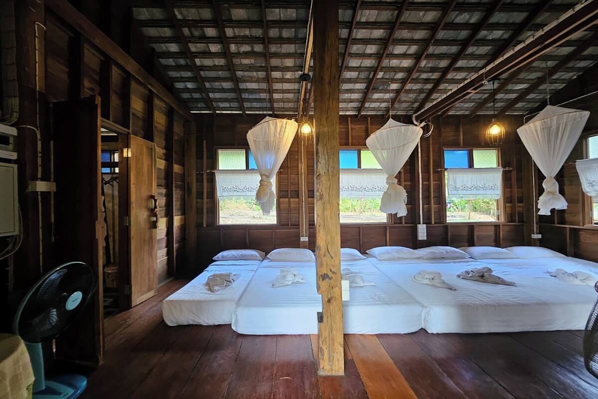 Ein Zimmer mit Holzwänden und schrägverdeckter Decke, ausgestattet mit drei Betten, die mit weißen Laken und Moskitonetzen bezogen sind.