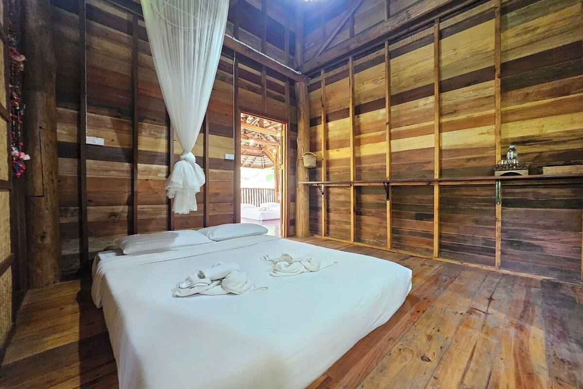 Ein Zimmer mit Holzboden, einem Bett, einem hängenden Baldachin und einem Regal mit einer Lampe.