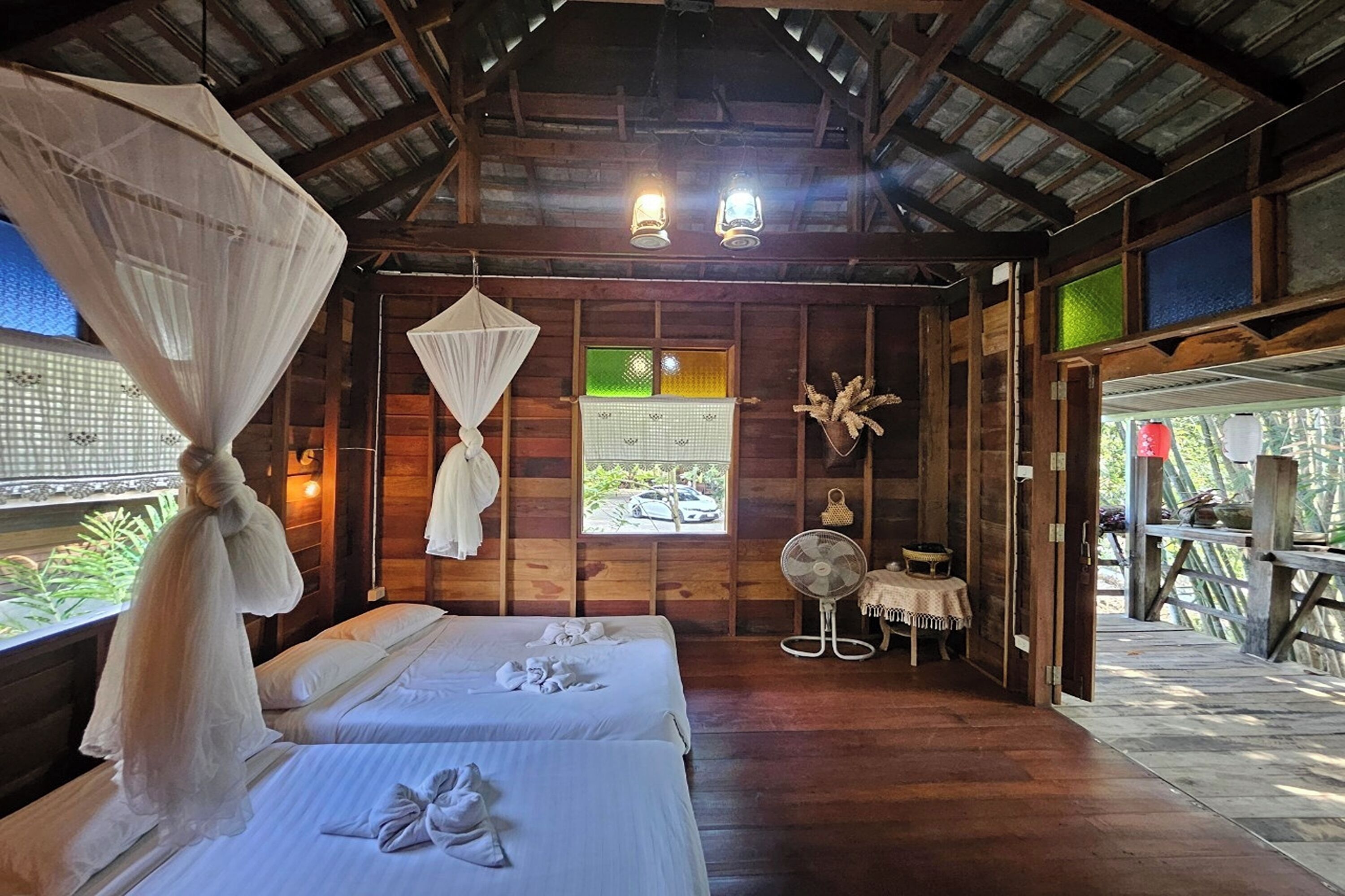 A wooden room with two beds, a fan, and a window with a view of the outside.