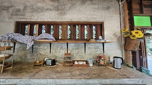 A rustic kitchen with a wooden shelf, a hanging basket with sunflowers, and various kitchen items.