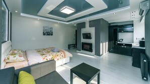Ett modernt hotellrum med en säng, en soffa och ett litet bord. Man kan se en öppen spis och ett litet köksområde.