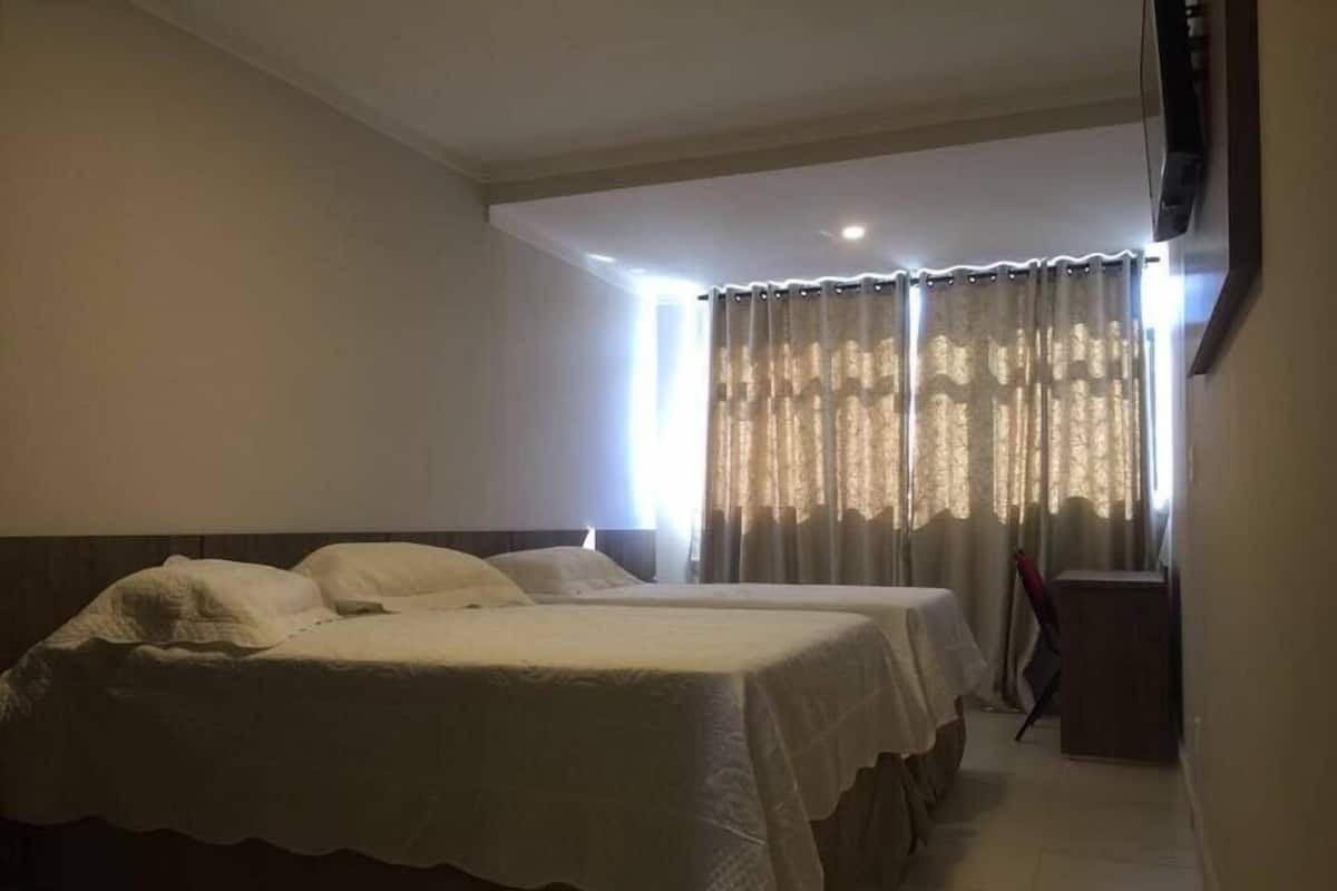 A hotel room with two beds, a television, and a window with curtains.