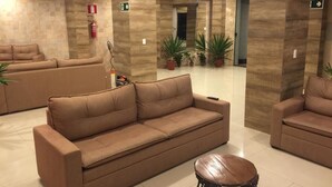 A spacious lobby with a beige sofa, a wooden coffee table, and potted plants. - Village Plaza Hotel (Barbacena)