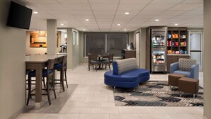 Uma sala de estar moderna com uma mesa de jantar, sofá azul e área de cozinha com geladeira e micro-ondas.