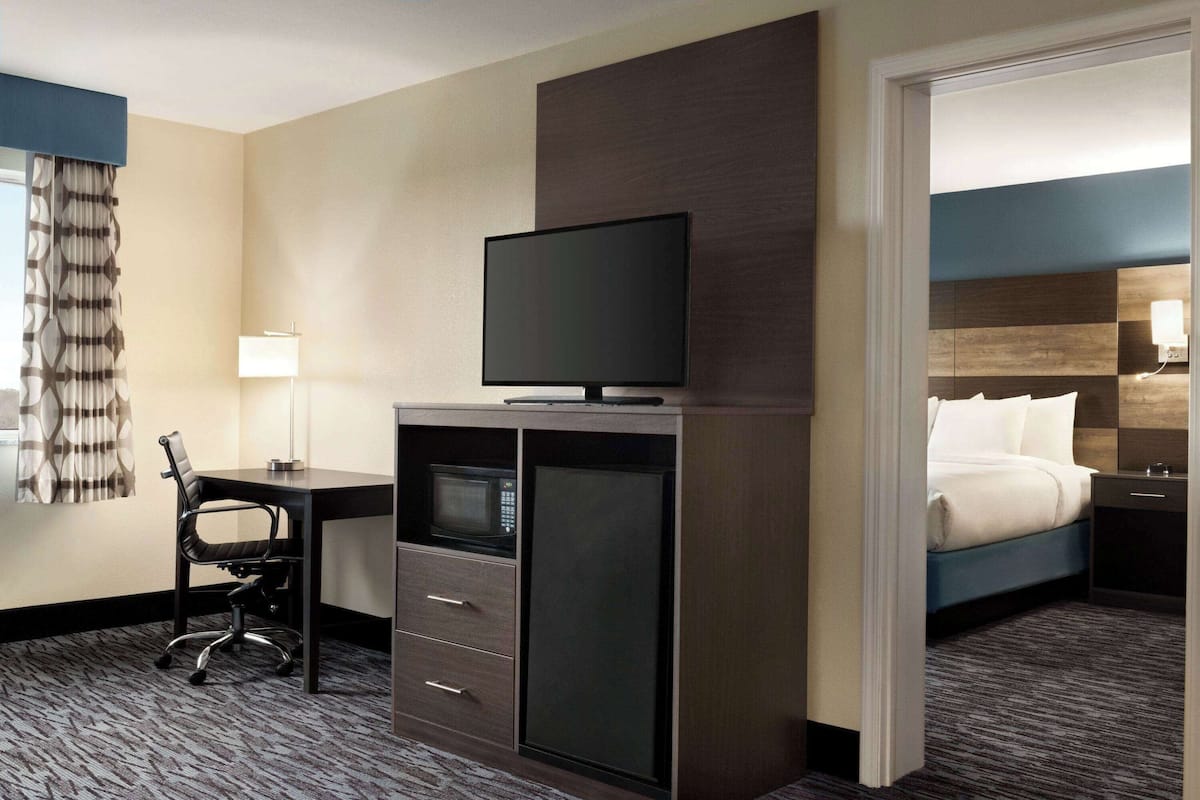 A hotel room with a flat-screen TV, a desk with a chair, a microwave, and a bed with a nightstand.