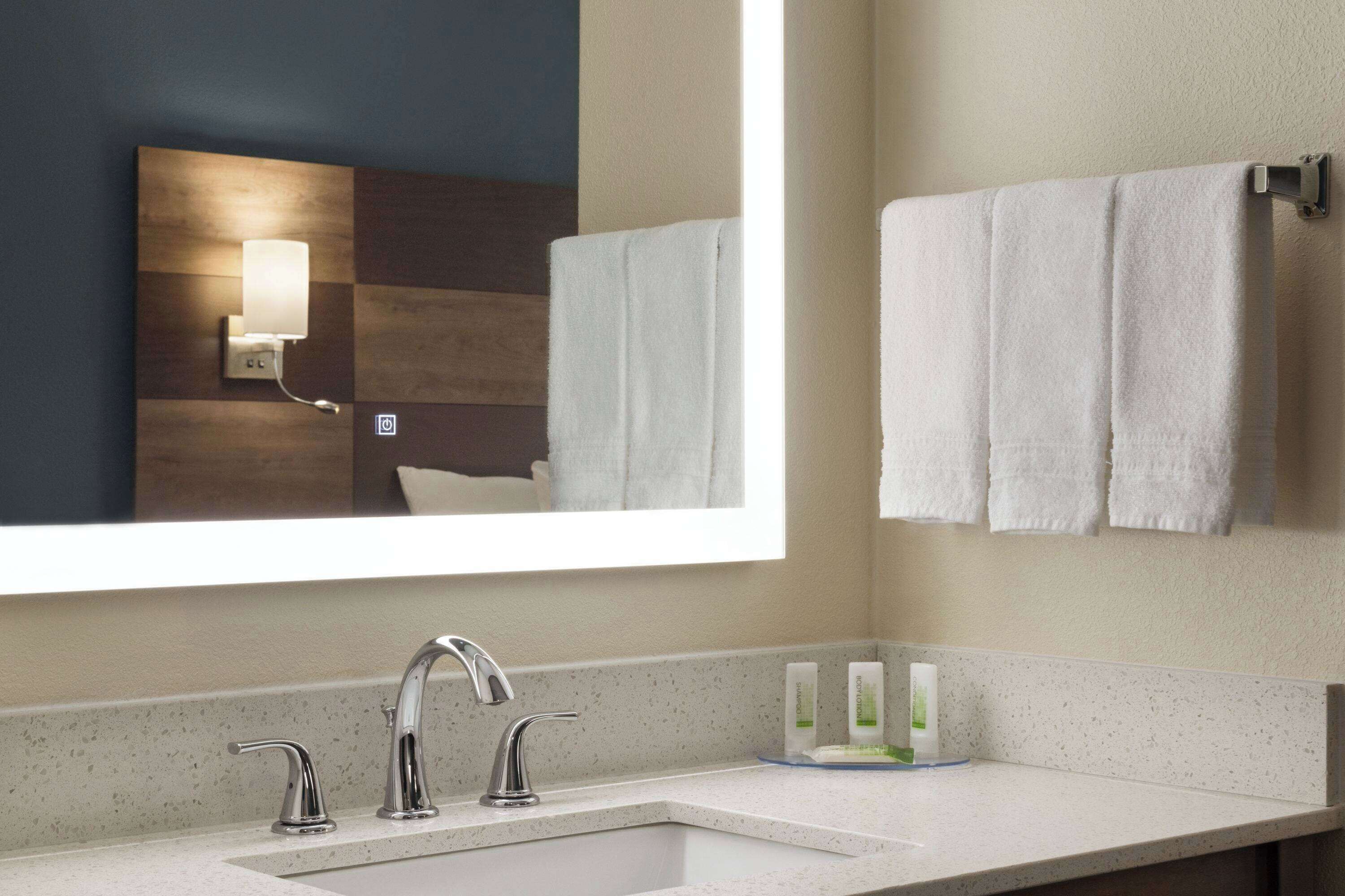 A modern bathroom with a large mirror, a sink with two faucets, and a towel rack with multiple towels.