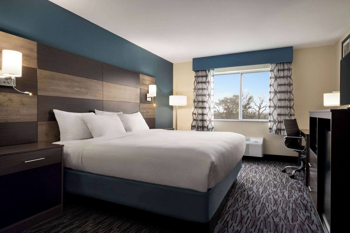 A hotel room with a large bed, a desk, a chair, and a TV.