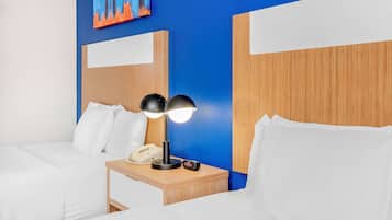 A hotel room with two beds, a wooden nightstand with a lamp, a phone, and a painting on the wall.