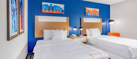 A hotel room with two beds, a blue accent wall, and artwork.