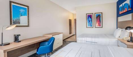 Una habitación de hotel con escritorio, una silla, una cama y dos cuadros en la pared.