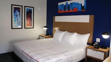 A hotel room with a large bed, two bedside tables, a night lamp, a wall-mounted painting, and a framed picture.