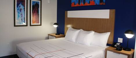 Habitación de hotel con una cama grande, dos mesitas de noche, una lámpara de noche, un cuadro en la pared y una fotografía enmarco.