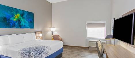 Une chambre d’hôtel avec un grand lit, un bureau, une chaise, une télévision et un tableau au mur.