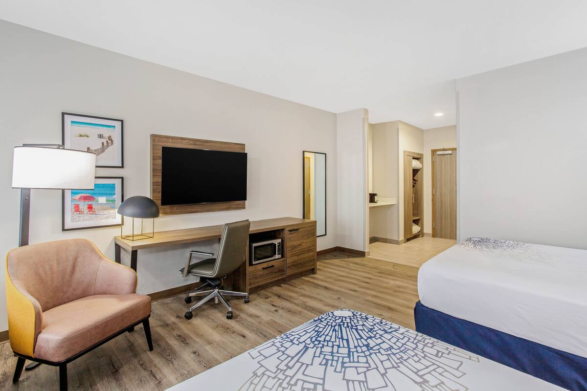 A hotel room with a bed, desk, chair, TV, and artwork on the wall.