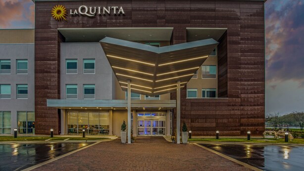Una entrada de hotel moderna con un letrero destacado, un vestíbulo cubierto y una fachada bien iluminada.