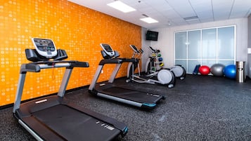 Un gimnasio con cintas de correr, un televisor montado en la pared y pelotas de ejercicio.