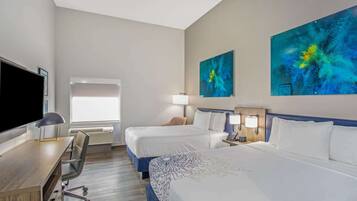A hotel room with two beds, a desk, a chair, a TV, and artwork on the walls.