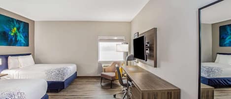 A hotel room with two beds, a desk, a chair, a TV, and artwork on the walls.