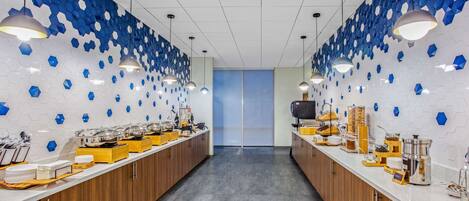A modern kitchen with a long counter, hexagonal blue tiles on the walls, and pendant lighting.