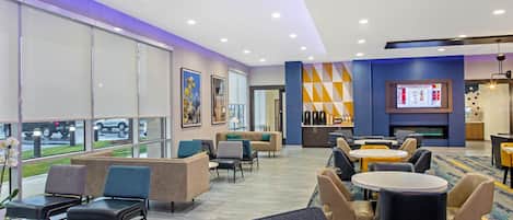 A hotel lobby with seating areas, a fireplace, and a television displaying a menu.