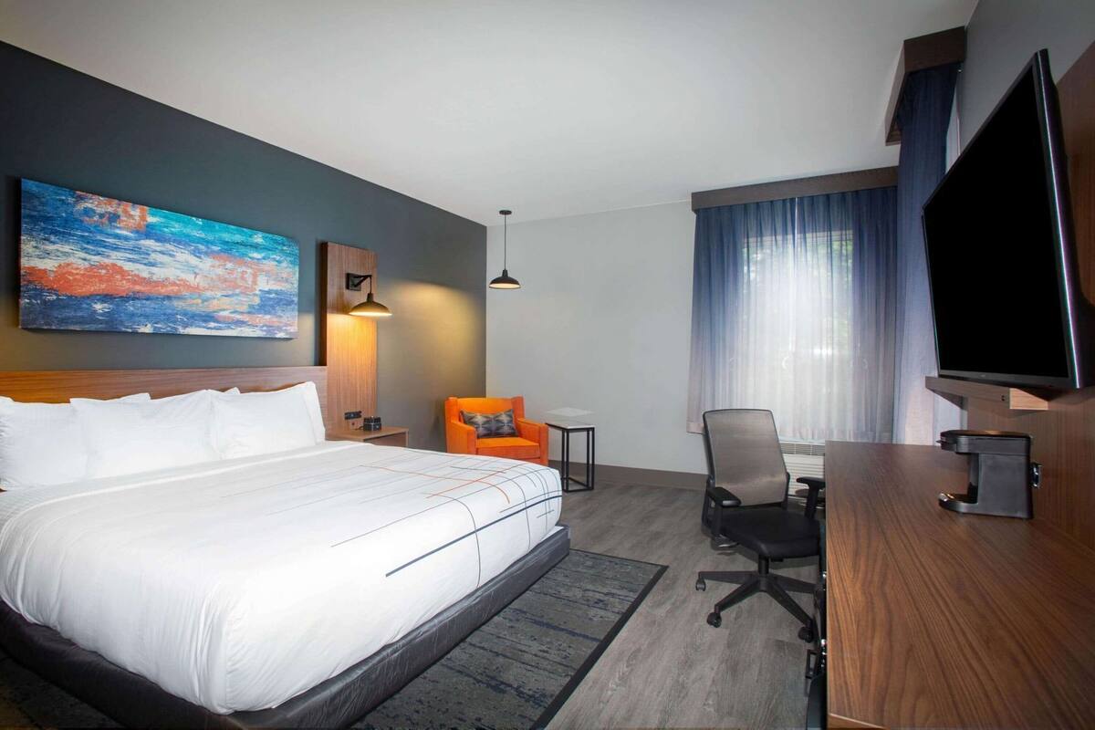 Une chambre d’hôtel avec un grand lit, un bureau avec une chaise, une télévision et un tableau au mur.