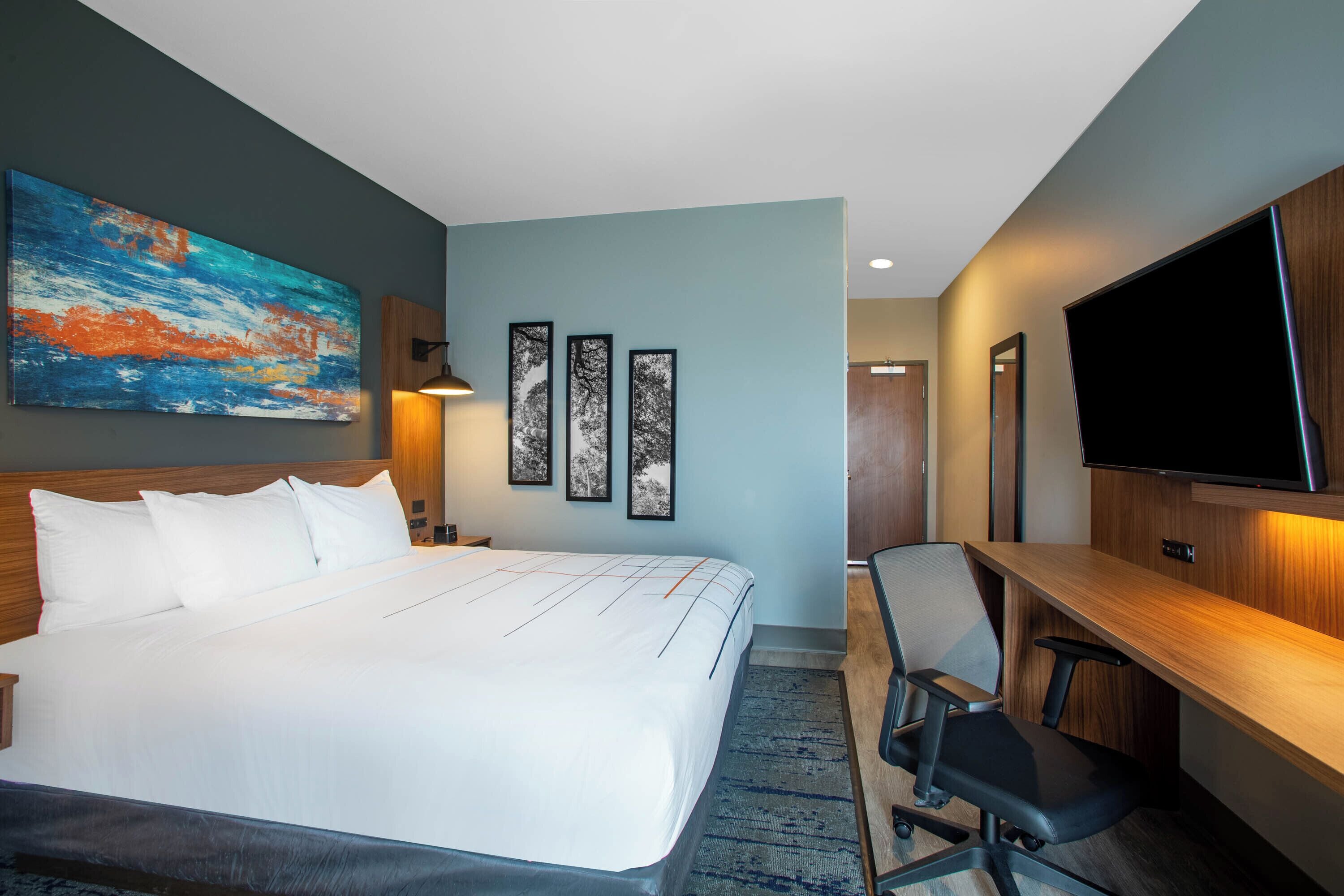 Une chambre d’hôtel dotée d’un grand lit, d’un bureau avec une chaise, d’un téléviseur à écran plat et d’œuvres d’art accrochées aux murs.