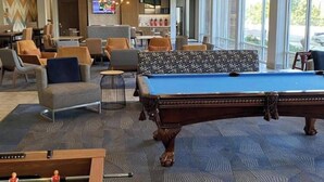Een biljart tafel, een tafelvoetbal tafel en een televisiescherm in een hotel lobby.