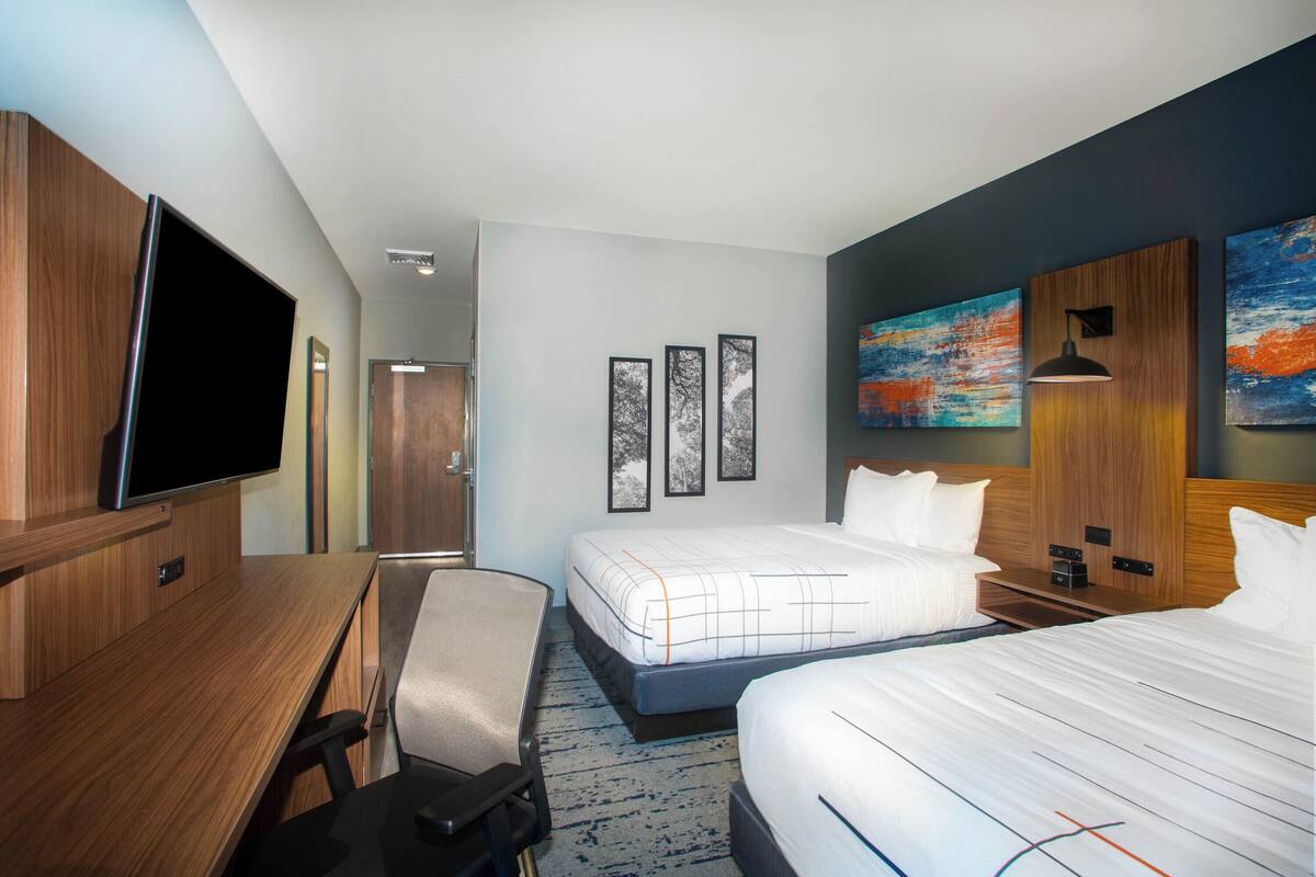 Une chambre d’hôtel équipée d’un lit, d’un bureau, d’une chaise, d’une télévision et décorée avec des œuvres d’art aux murs.