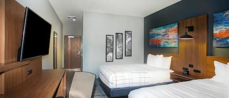 A hotel room with a bed, a desk, a chair, a TV, and artwork on the walls.