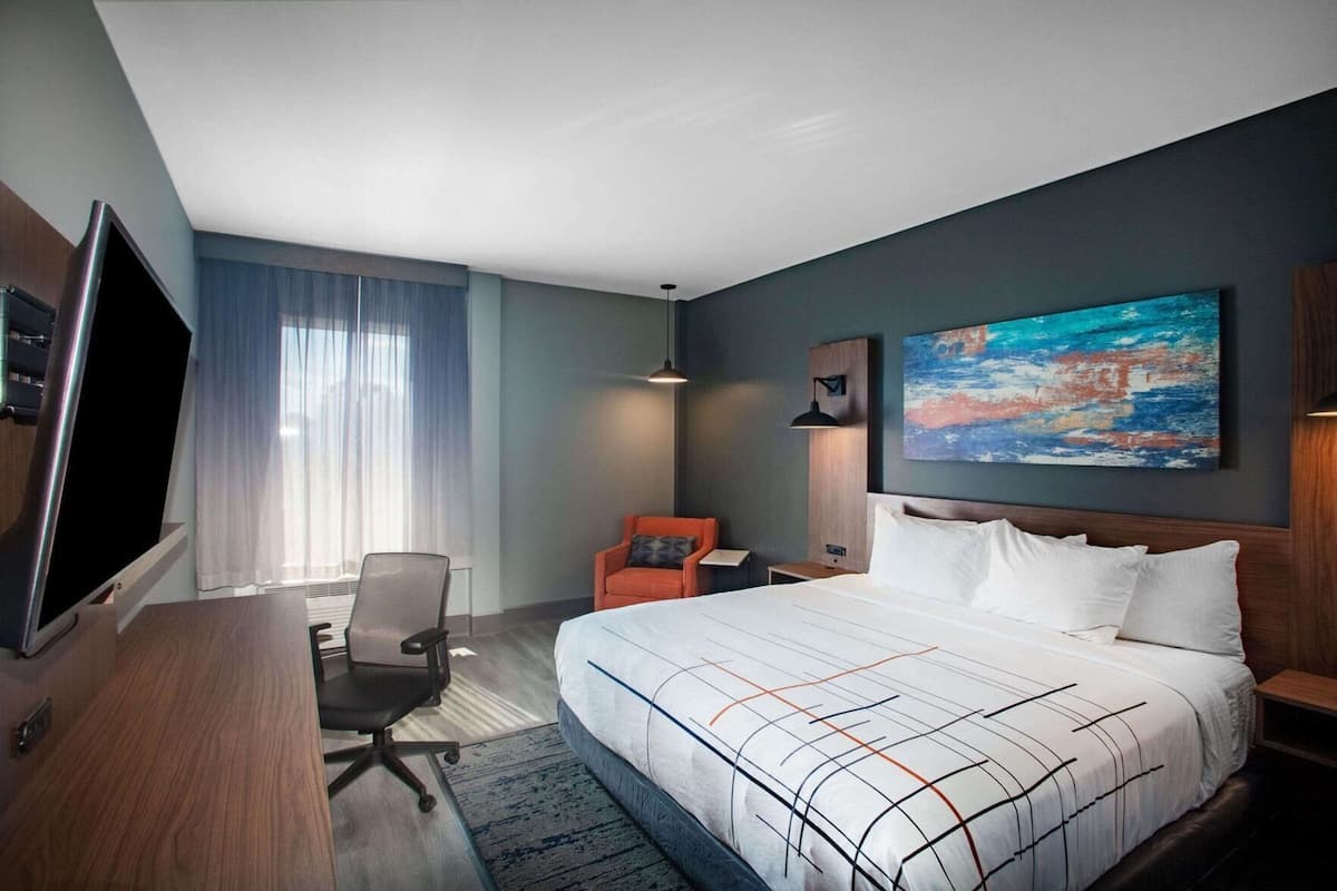 Une chambre d’hôtel avec un lit, un bureau, une chaise, une télévision et un tableau au mur.